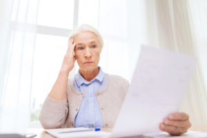 A stressed older woman with her hand to her head is looking at a piece of paper