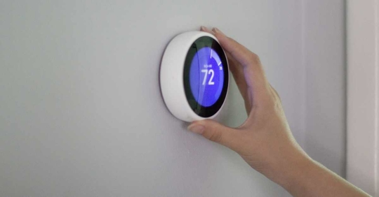 A hand adjusting a smart thermostat on a white wall.