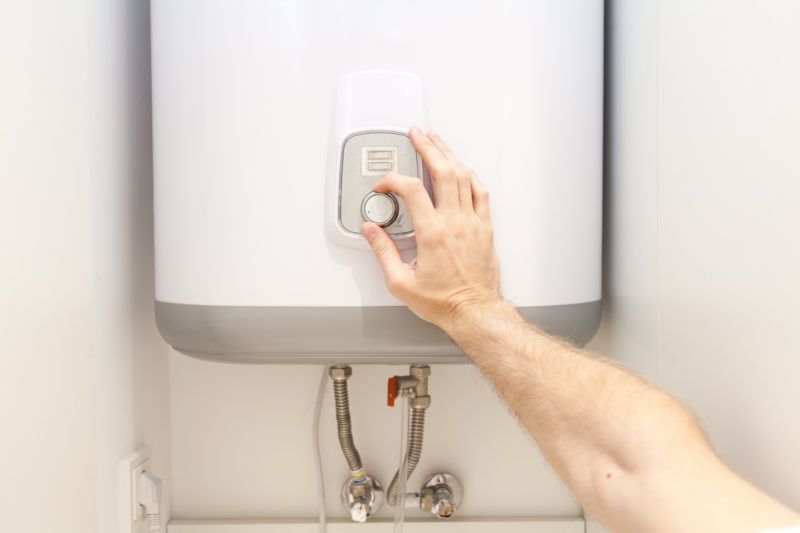 A hand adjusting the thermostat on a white tankless water heater