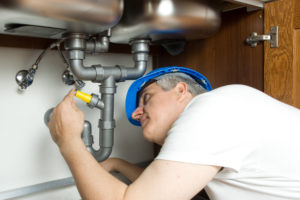 A plumber in a blue hat checking the pipes under a sink