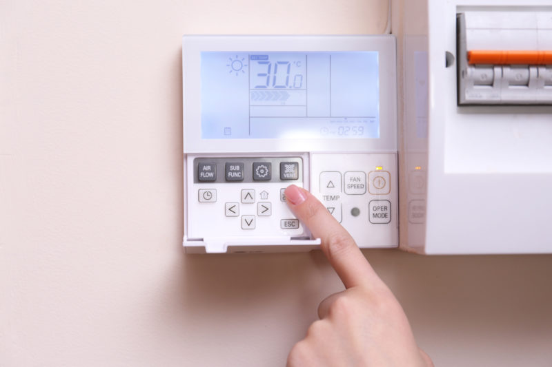 A white programmable thermostat with a finger pressing a button