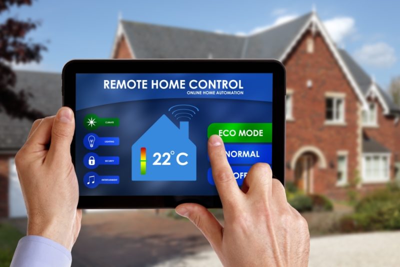Remote Home Control app on a tablet outside a brick house. A hand is setting the eco mode button. 