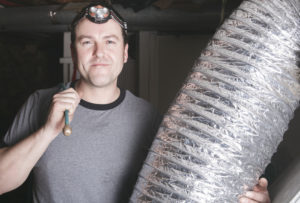 A Lubbock HVAC contractor holding ductwork and a tool in his left hand
