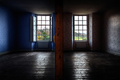 Two dark rooms with wood floors and windows with heating units under them