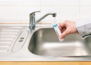 A person filling a tube with water from a kitchen faucet
