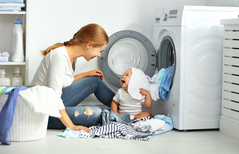 A mother and her laughing baby playing with clothes fresh out of the dryer