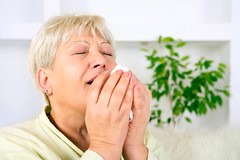 A blonde woman sneezing into a tissue