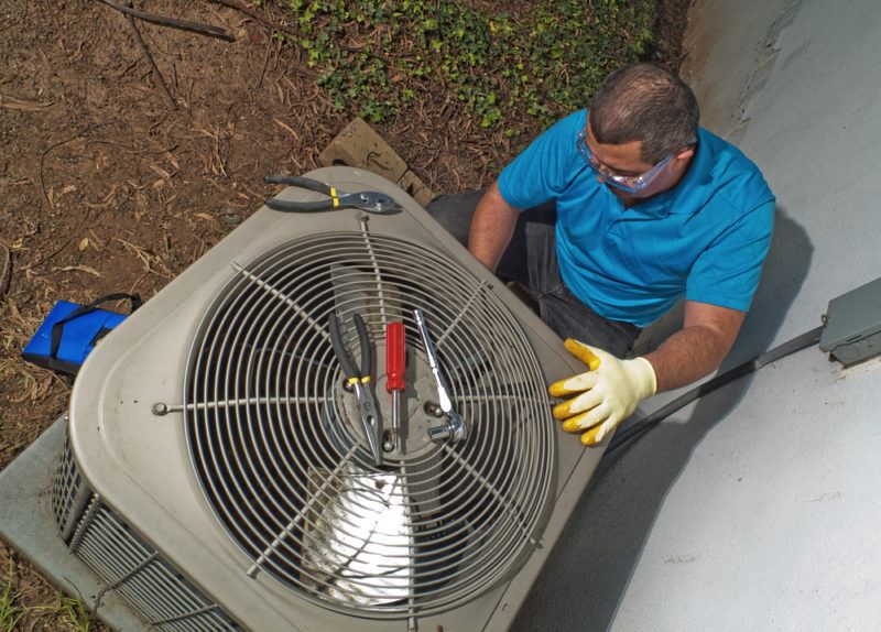 A Lubbock HVAC technician in a blue shirt and wearing clear safety goggles adjusting an outdoor HVAC unit