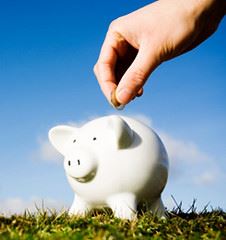 A hand placing coins into a white piggy bank