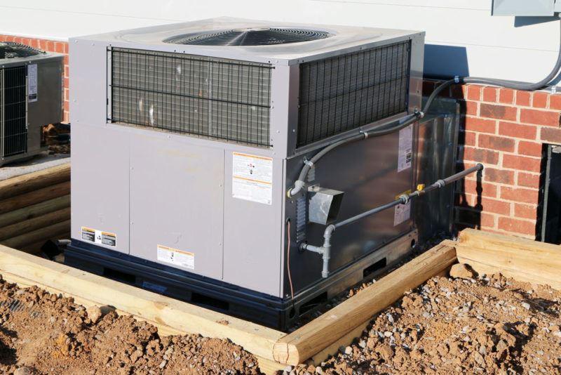 Packaged HVAC unit in a wooden enclosure against a brick wall