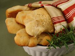 Parmesan rosemary breadsticks in a white bowl with a sprig of rosemary and a red, white, and beige cloth around them